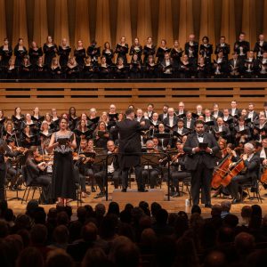 Large choir and orchestra performing onstage with a conductor