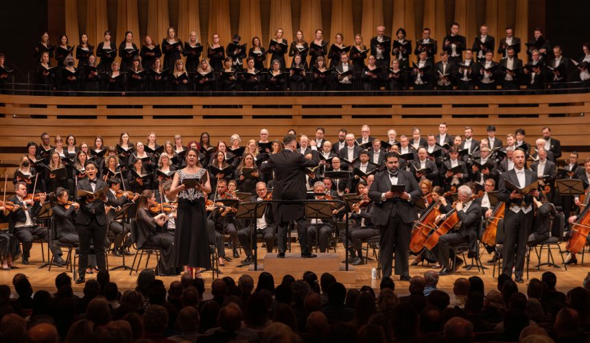 Large choir and orchestra performing onstage with a conductor